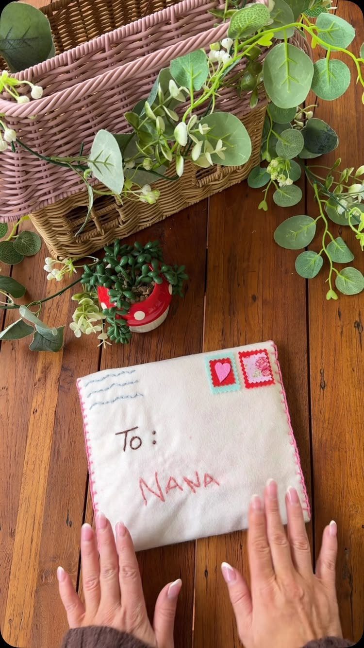 White felt envelope with embroidered text and heart held by two hands.