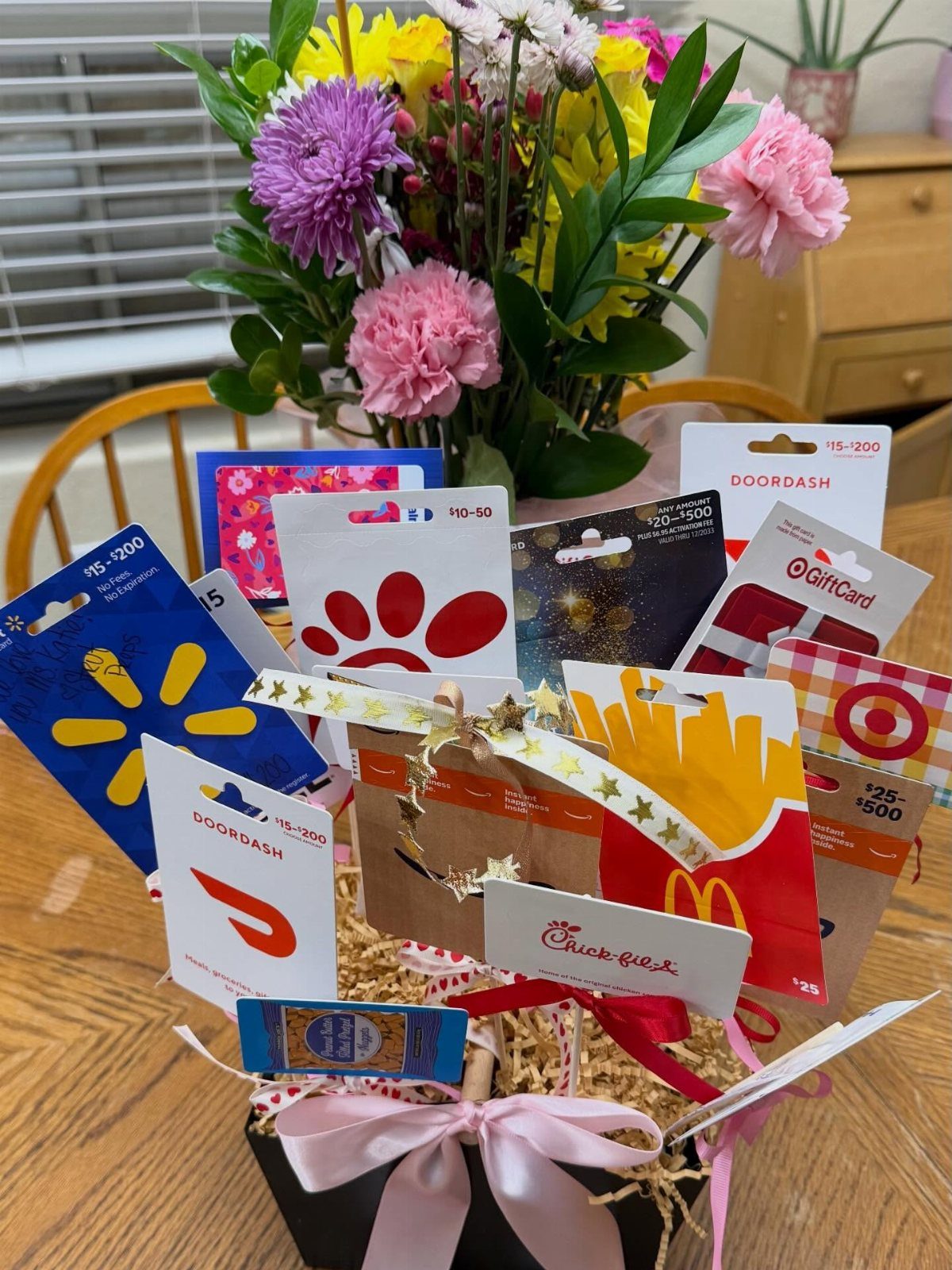 Gift cards arranged in a decorative pot with a pink bow and flowers.