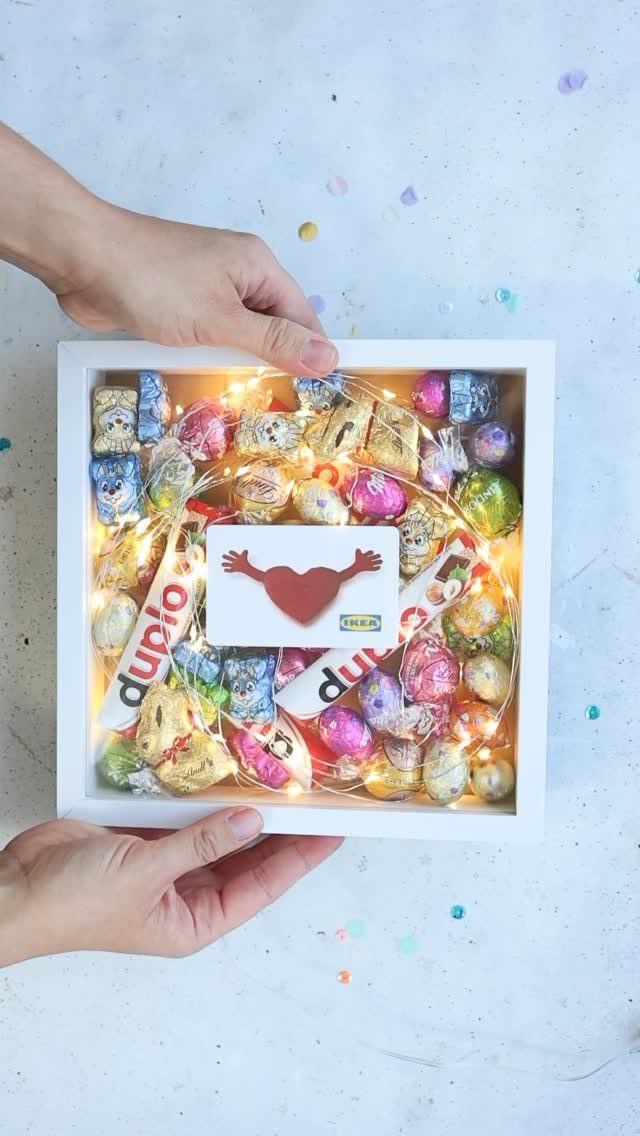 White shadow box frame filled with colorful candies, fairy lights, and a gift card.