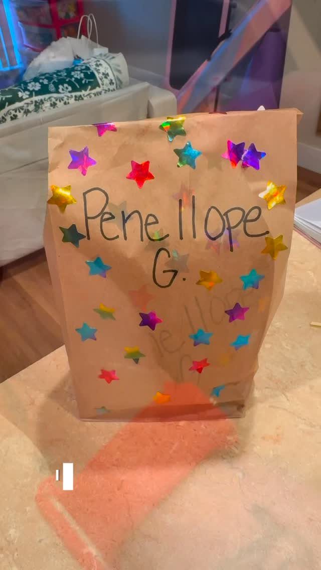Brown paper lunch bag decorated with colorful star stickers and a handwritten name.