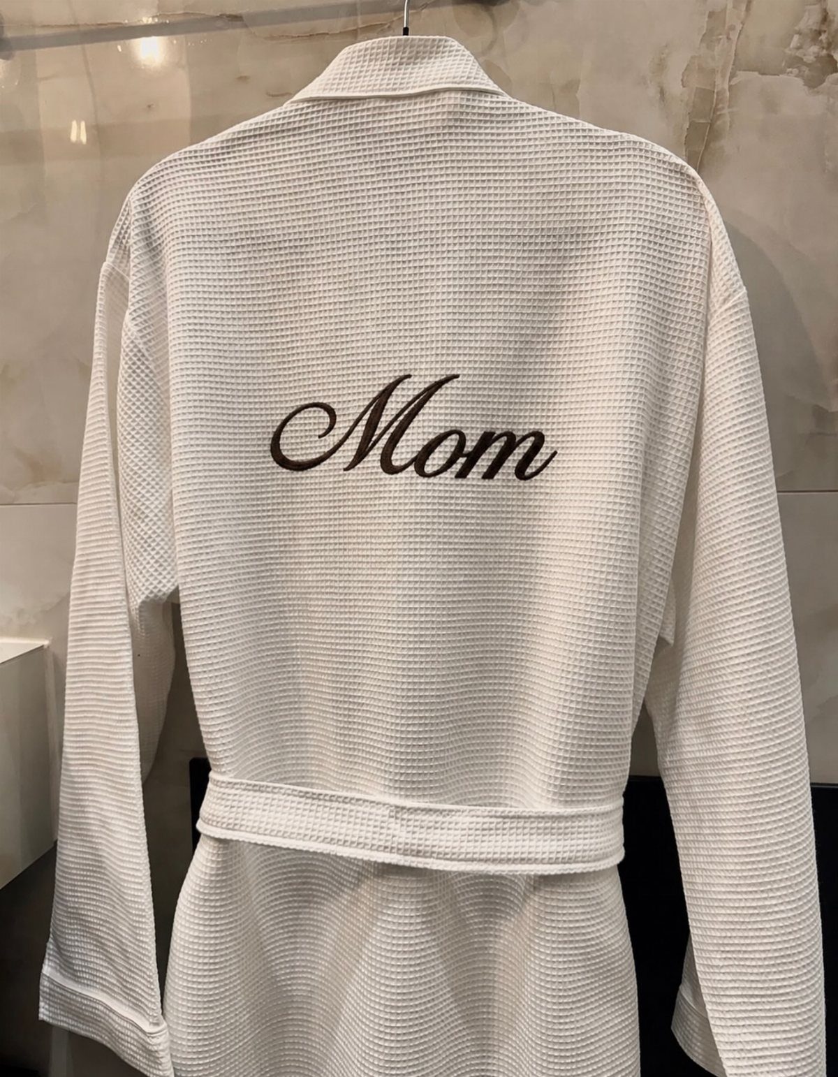 White waffle-weave bathrobe with Mom embroidered in brown cursive on the back.