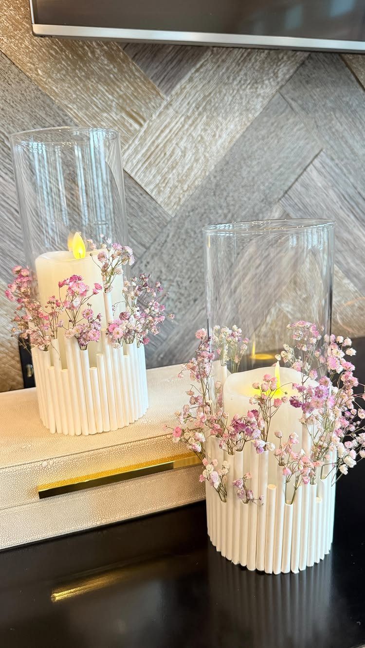 White ribbed candle holders with pink flowers and lit pillar candles in glass cylinders.