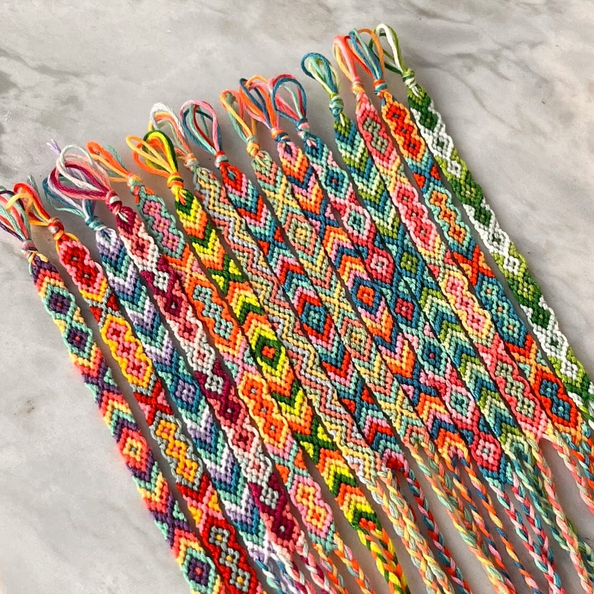 Colorful hand-woven friendship bracelets with geometric patterns on a white marble background