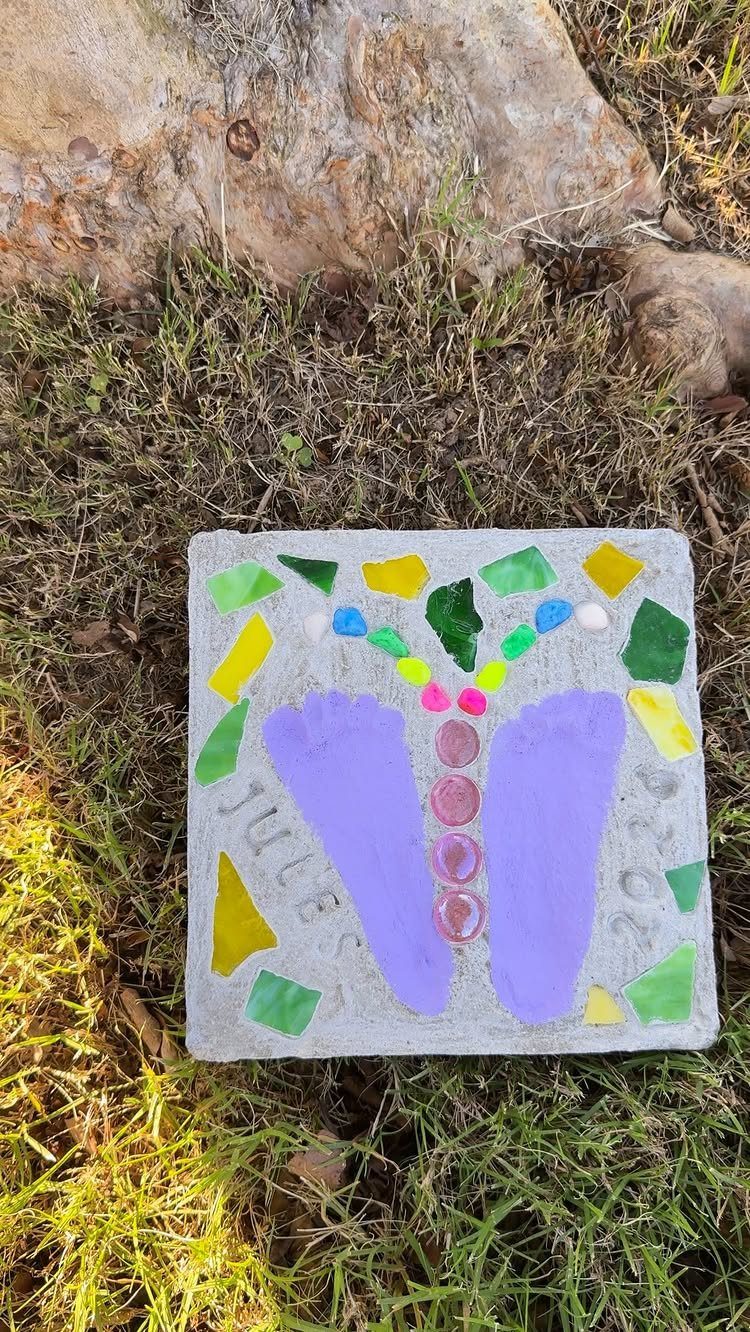 Concrete garden stepping stone with purple footprints, the name Jules, and colorful glass.