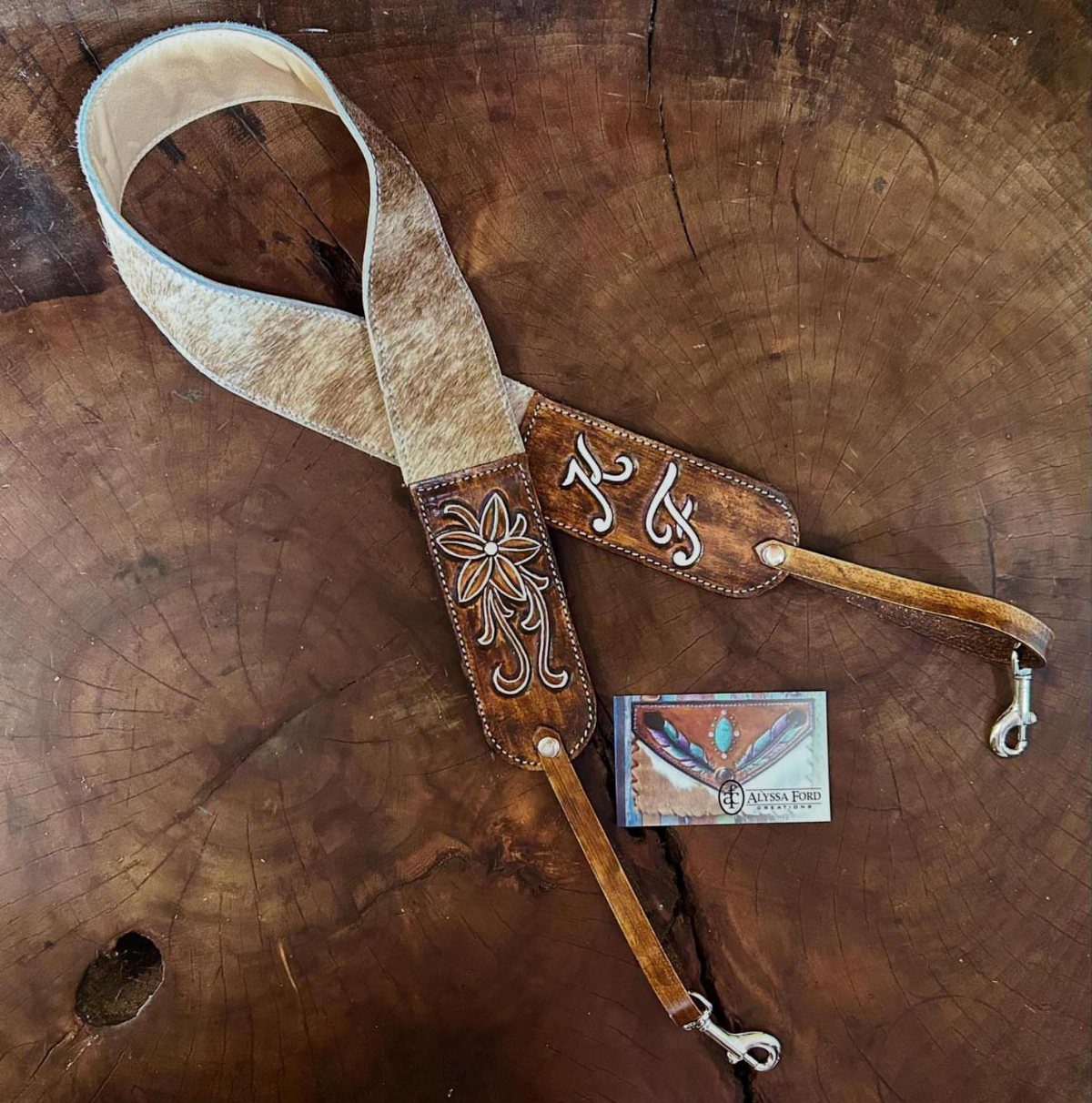 Leather camera strap with embossed floral designs resting on a wooden tree stump.