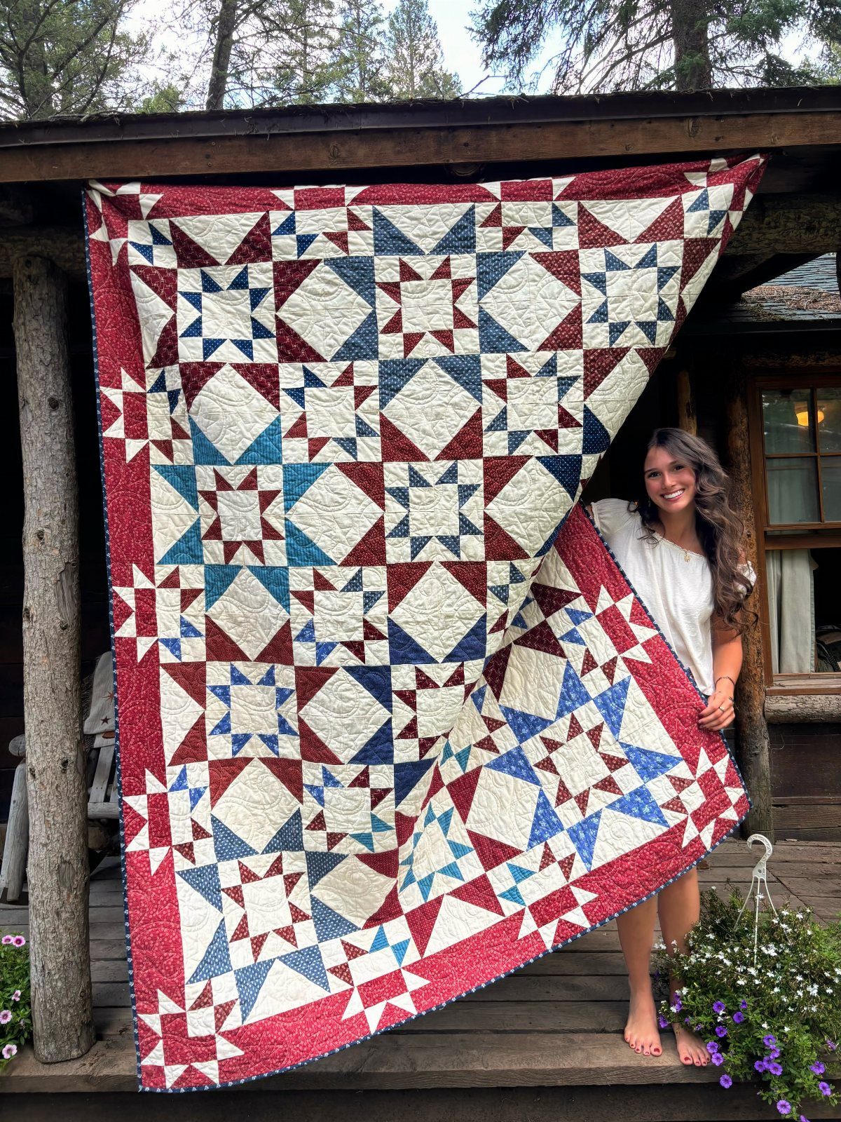 Woman holding a handmade red, white, and blue star pattern quilt on a porch