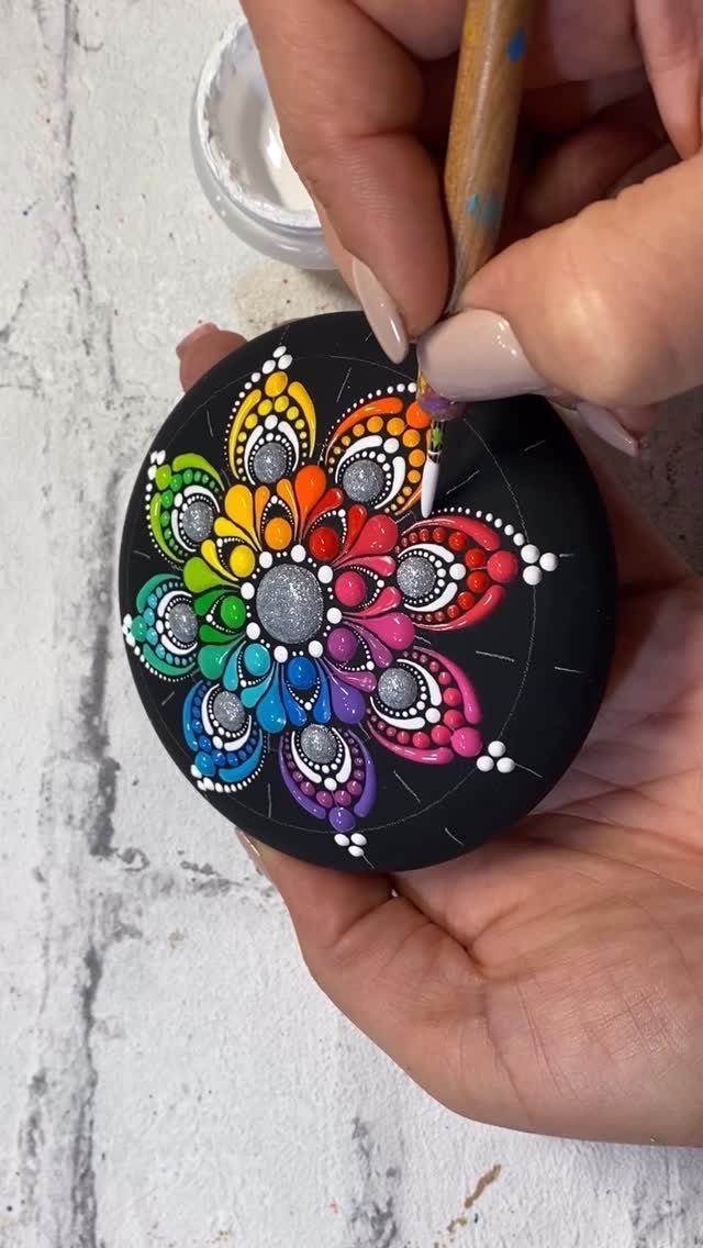 Hands painting a colorful dot mandala pattern on a black circular stone.