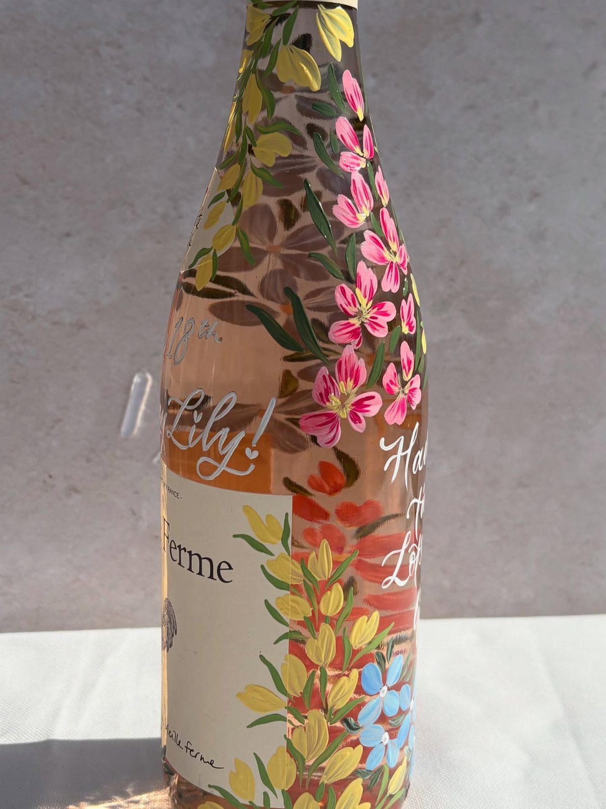 Painted wine bottle with colorful floral designs and handwritten white text on glass