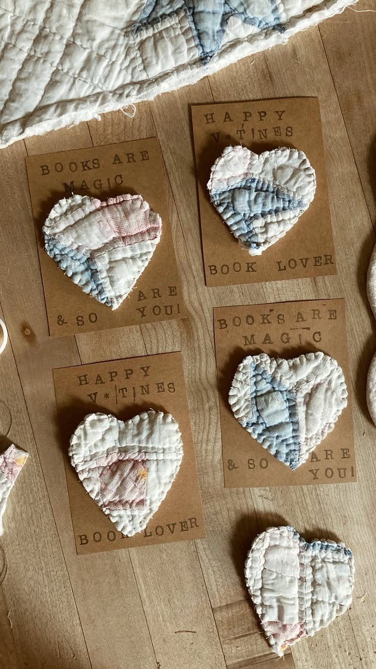 Heart-shaped quilted fabric patches on brown cardboard cards resting on a wooden surface.