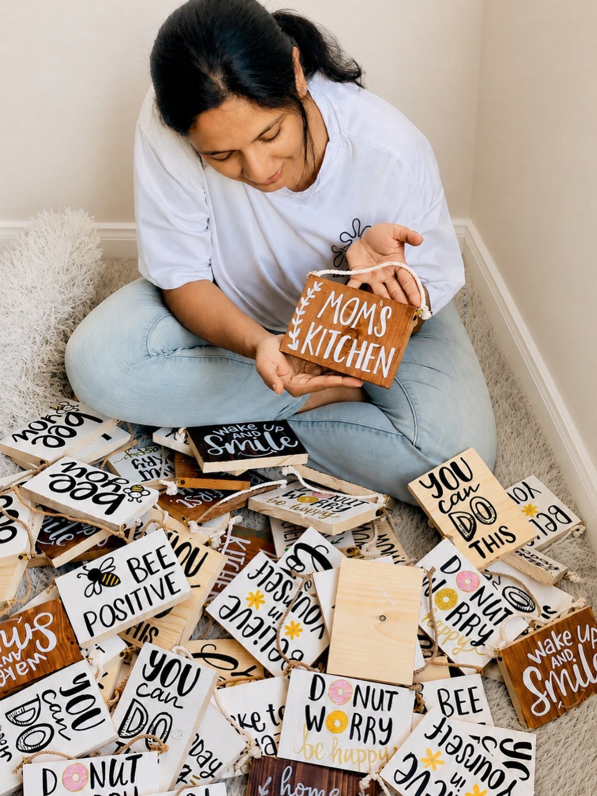 Woman holding a wooden Moms Kitchen sign surrounded by motivational wooden plaques