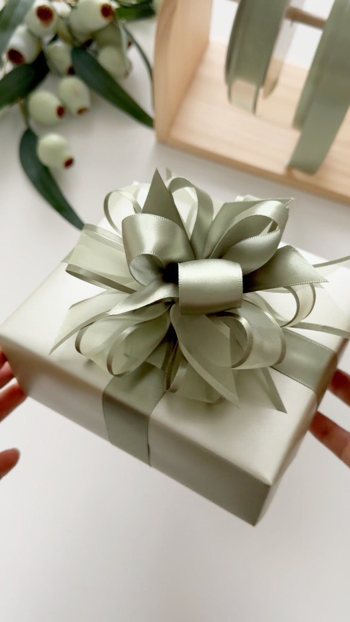 Champagne wrapped gift with a large sage green satin bow held by hands