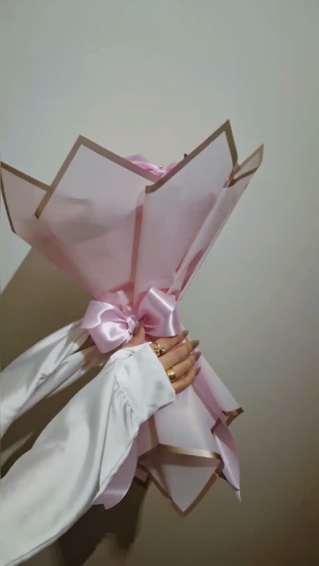 Pink wrapped bouquet with gold edges tied with a pink satin ribbon bow.
