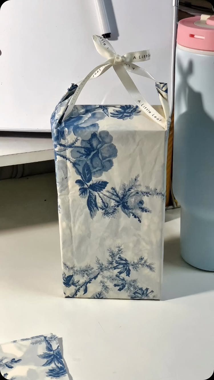 Blue floral wrapped gift with a white ribbon handle and small bow.