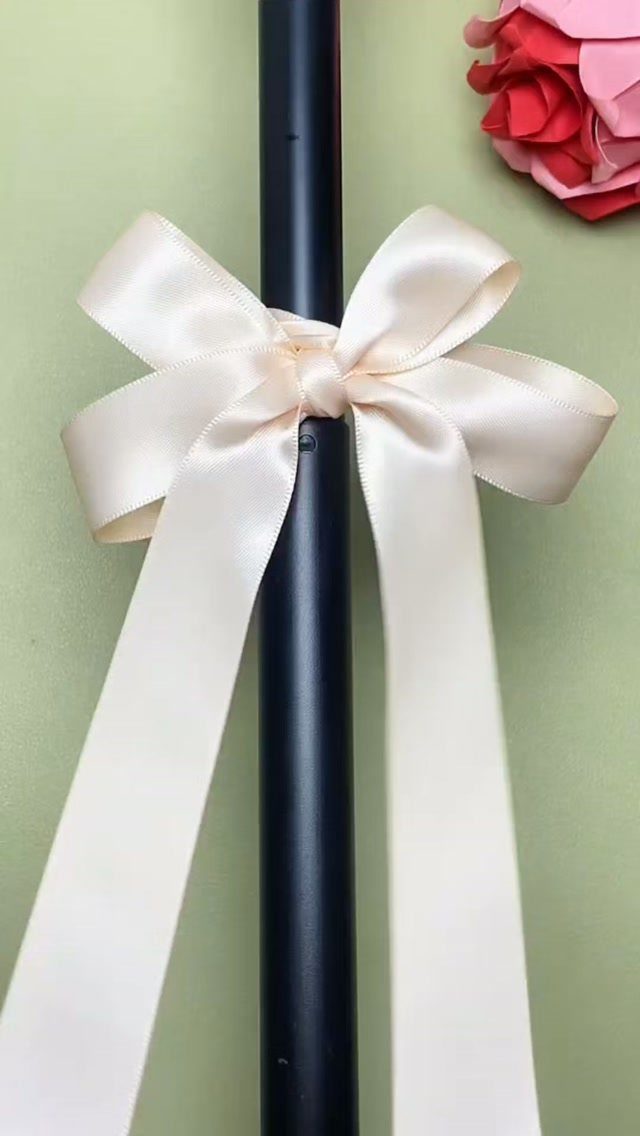 Black cylindrical bottle tied with a cream satin ribbon bow on green background