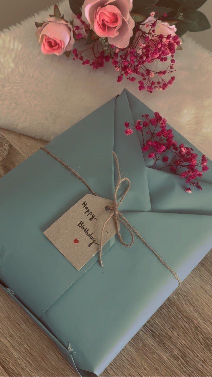 Blue wrapped gift with brown twine and a Happy Birthday tag near pink roses