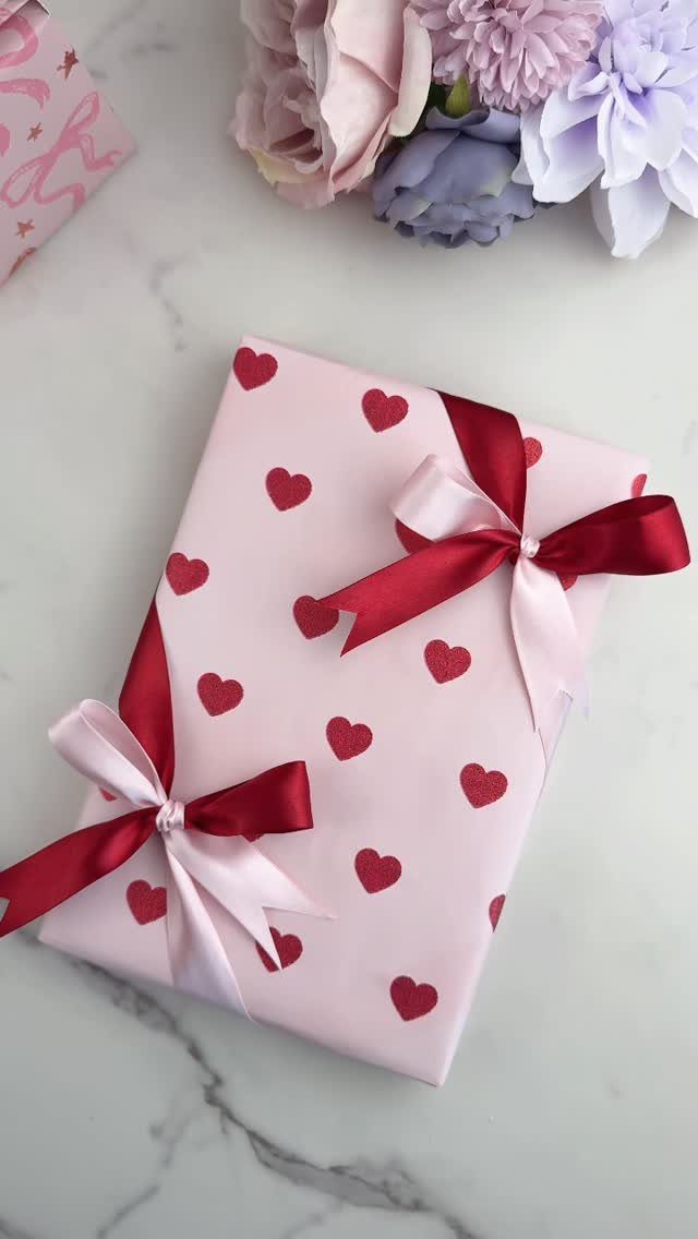 Pink heart-patterned gift wrapped with layered red and pale pink ribbons and bows.