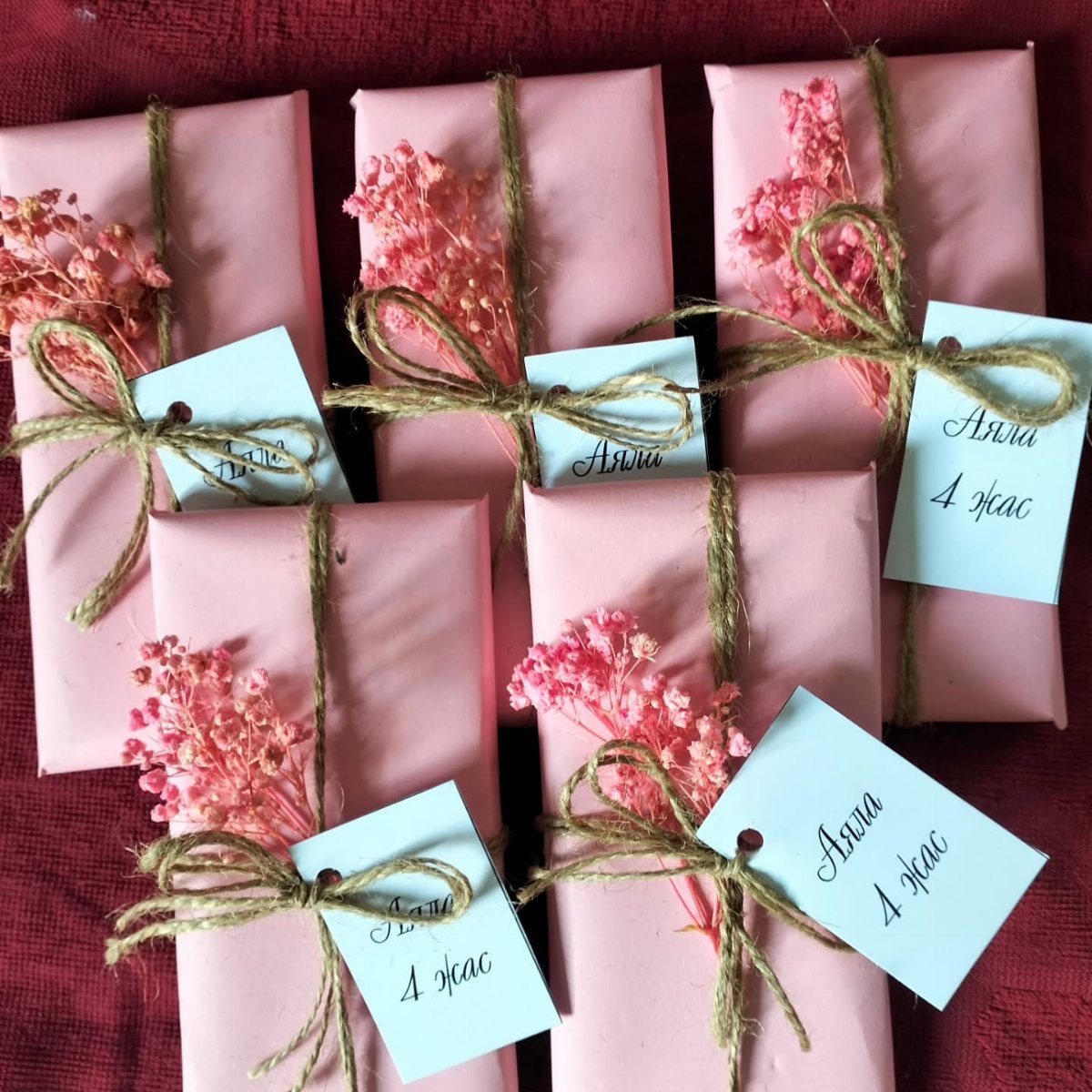 Pink wrapped gifts tied with twine, dried flowers, and blue name tags.