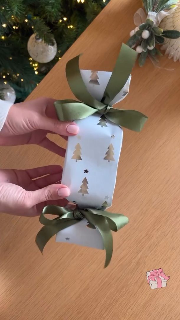 White gift wrapped with gold trees and olive green satin bows held by hands