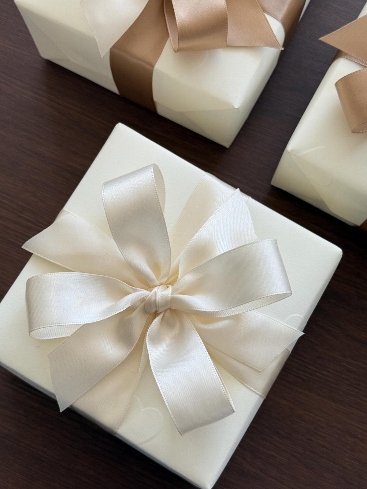 Cream wrapped gift boxes with a large satin bow on dark wood