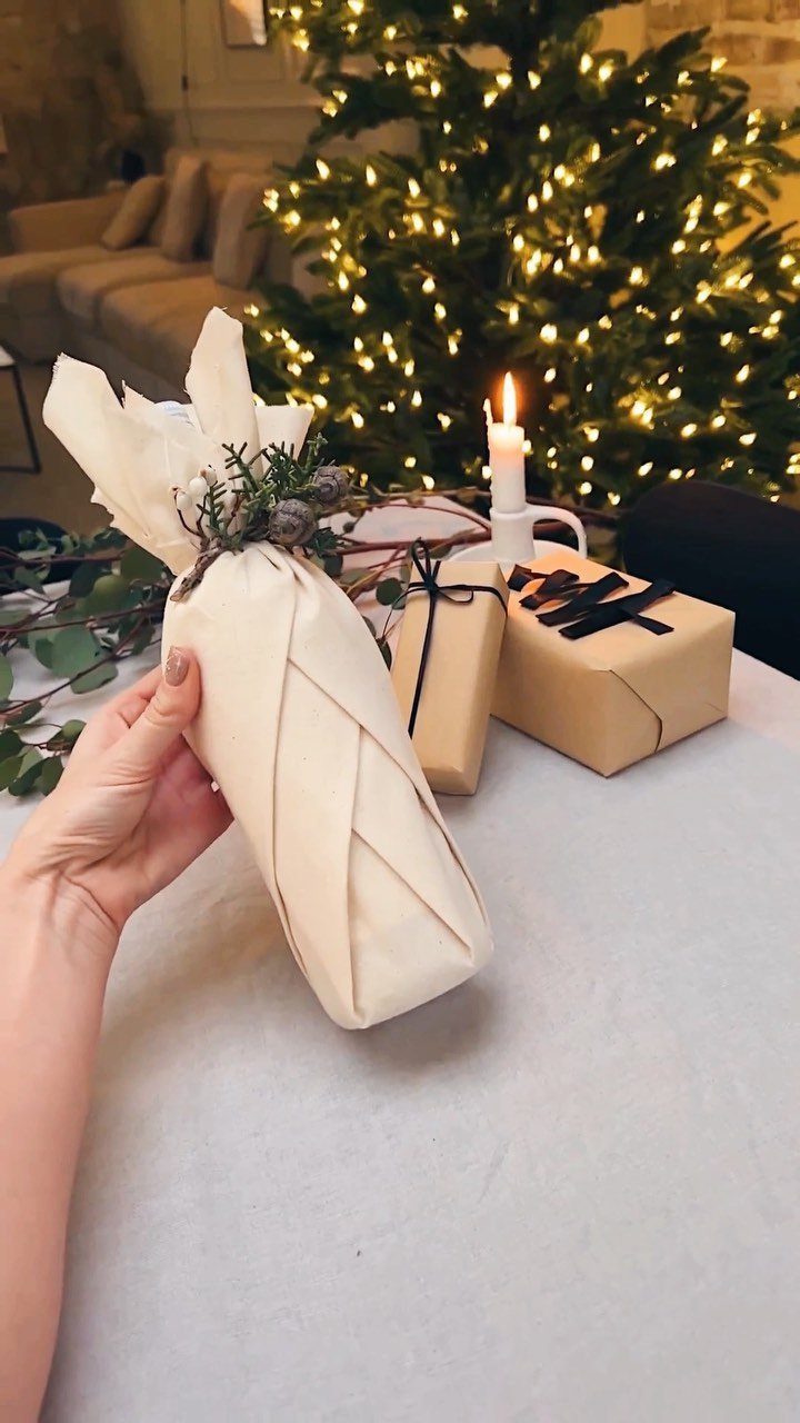 Bottle wrapped in cream fabric with a greenery accent held by a hand.