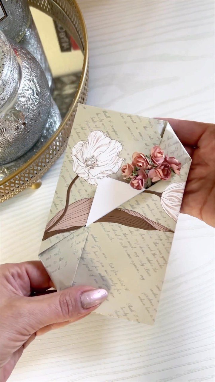 Hands holding a small floral paper envelope used for wrapping a gift card.