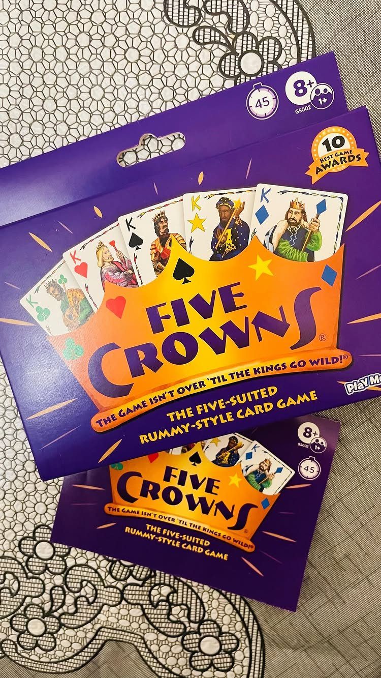 Five Crowns card game box and card resting on a white lace tablecloth.