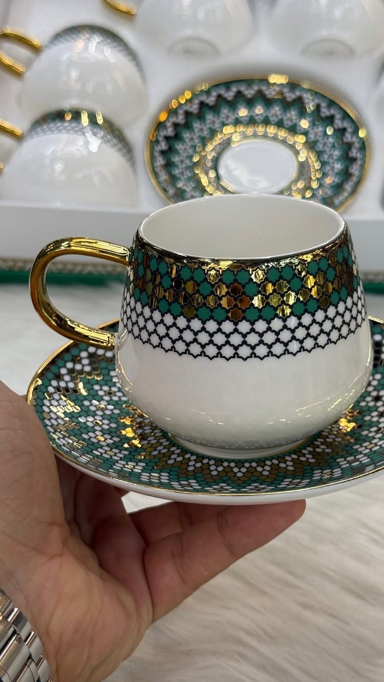 White ceramic coffee cup and saucer with teal and gold geometric patterns.
