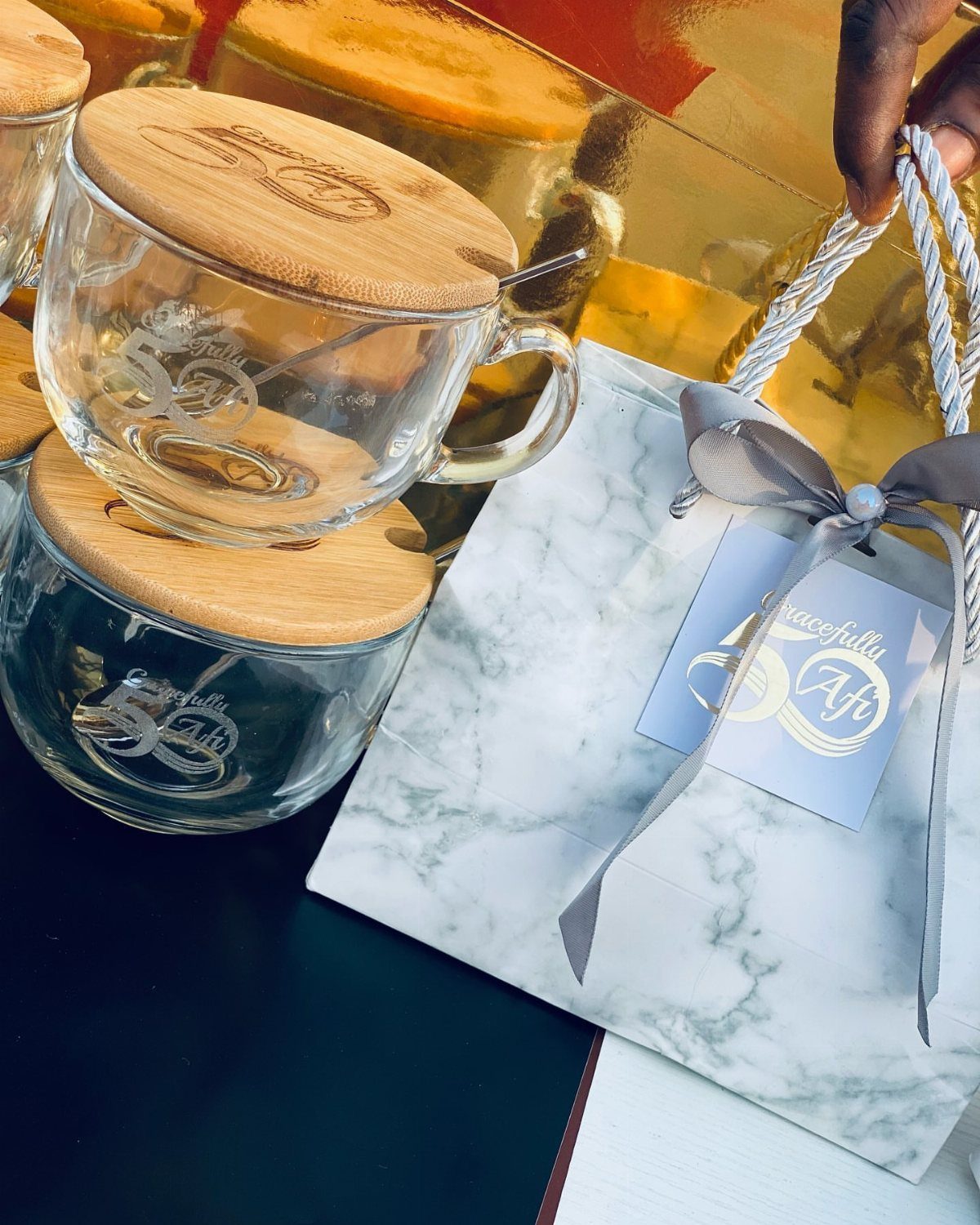 Clear glass mugs with wooden lids next to a marble-patterned gift bag.