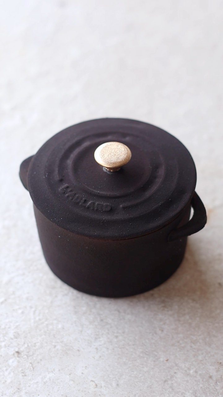 Small black cast-iron pot with a lid and gold knob on stone surface