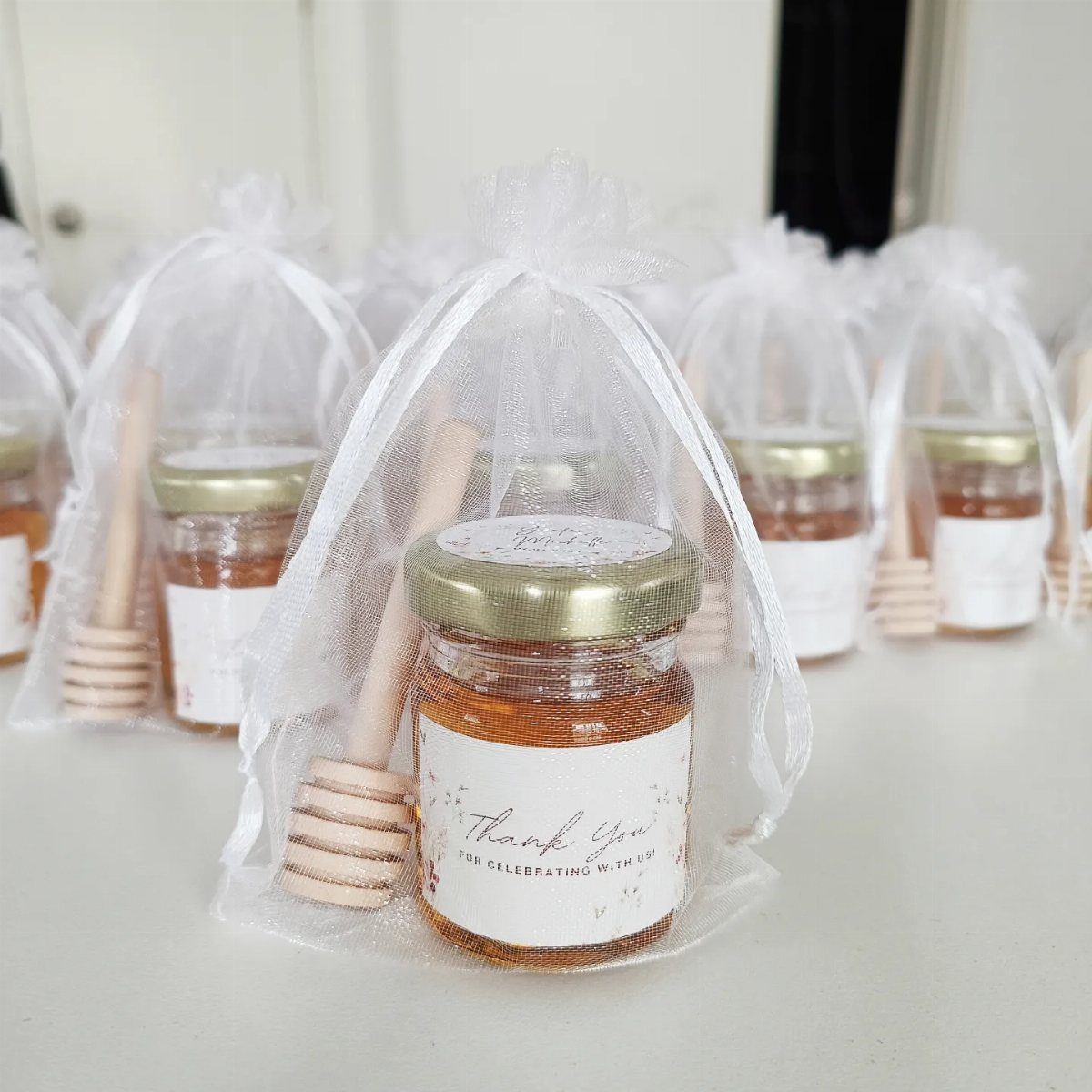 Small honey jars with wooden dippers in white organza gift bags.