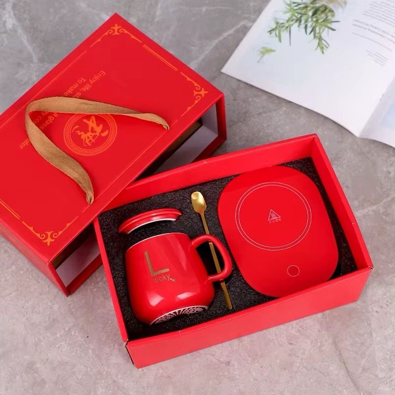 Red gift set with a mug, gold spoon, and warming pad in a box