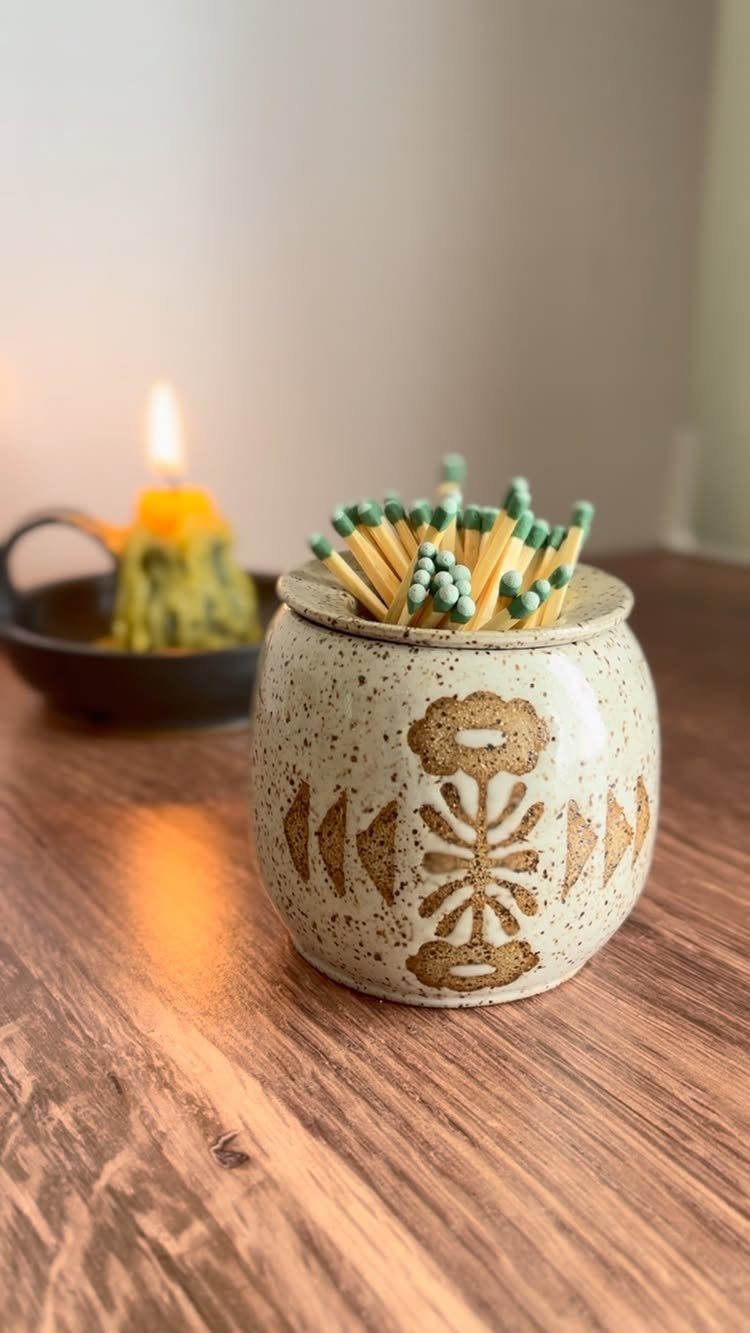Speckled ceramic match holder with green-tipped matches on a wooden table.