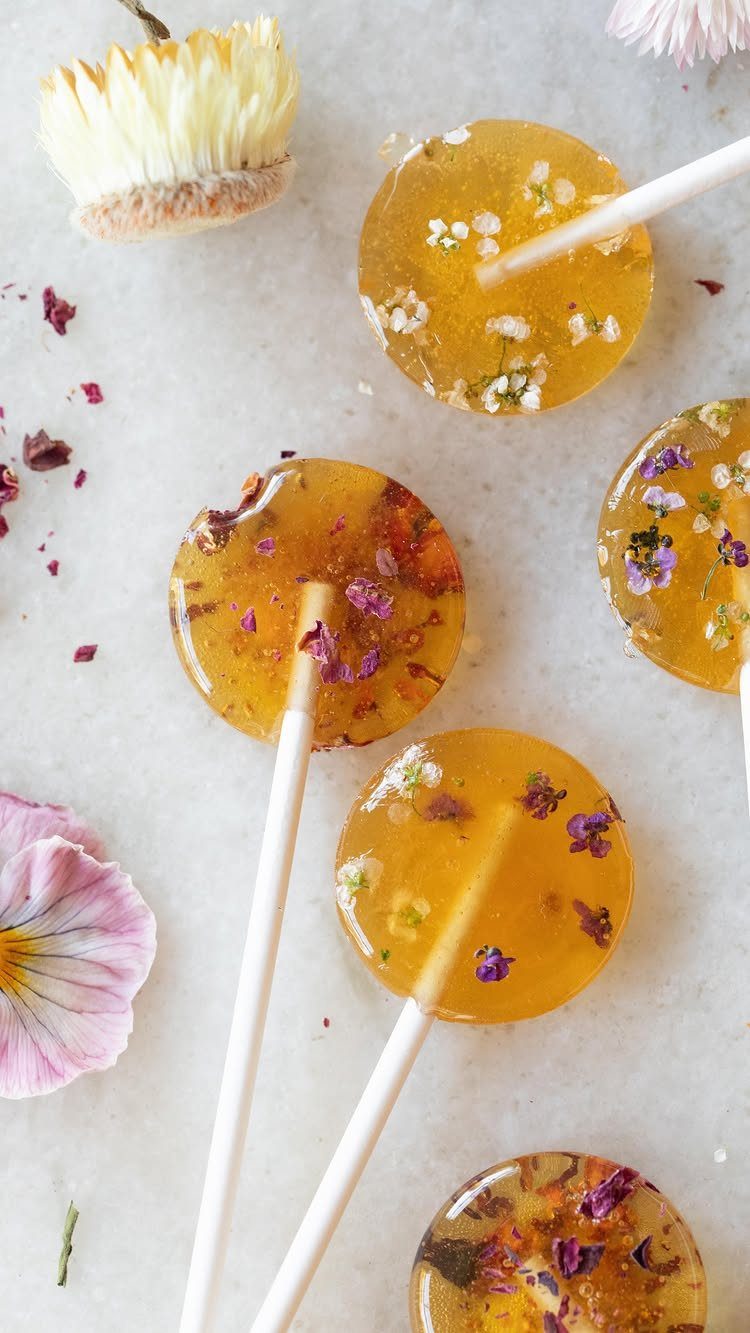 Amber lollipops with dried flower petals on a light grey stone surface.