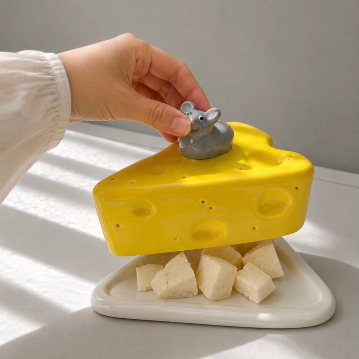 Yellow ceramic cheese-shaped lid with a grey mouse revealing cheese cubes on a plate