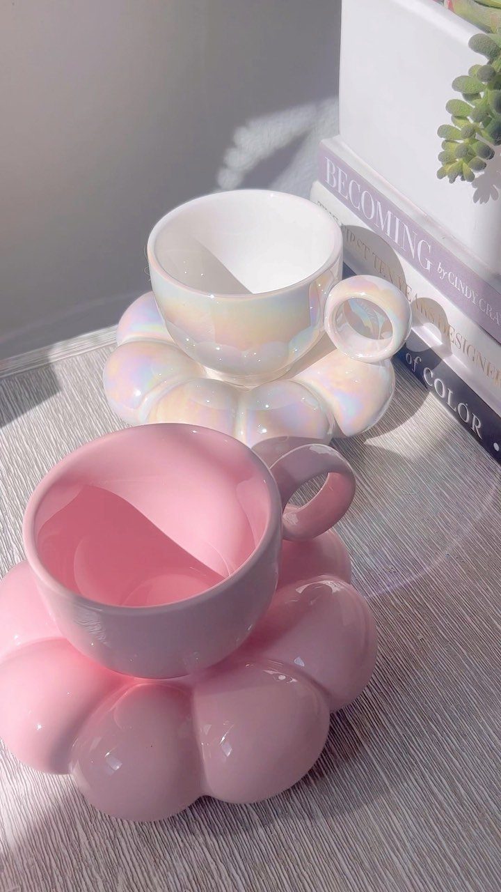 Two small ceramic cups in iridescent white and pink on scalloped saucers.