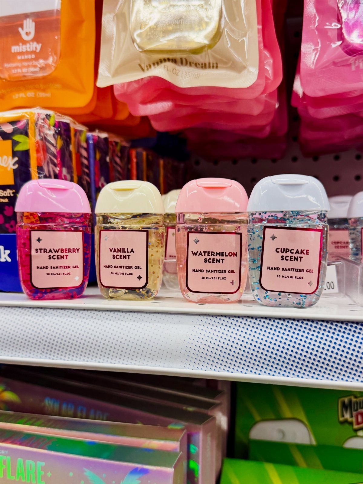 Four glittery hand sanitizer bottles with colorful lids on a white retail shelf.