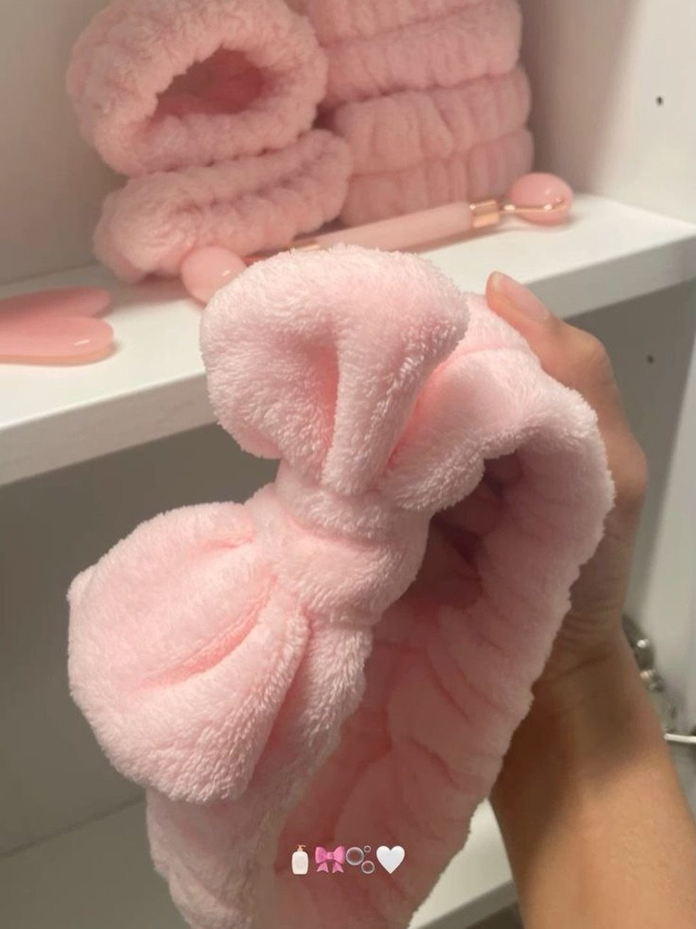 Pink plush spa headband with a bow held in a person's hand.