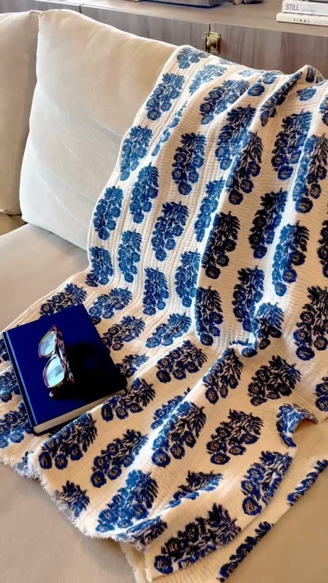 White throw blanket with blue floral patterns draped over a white sofa.