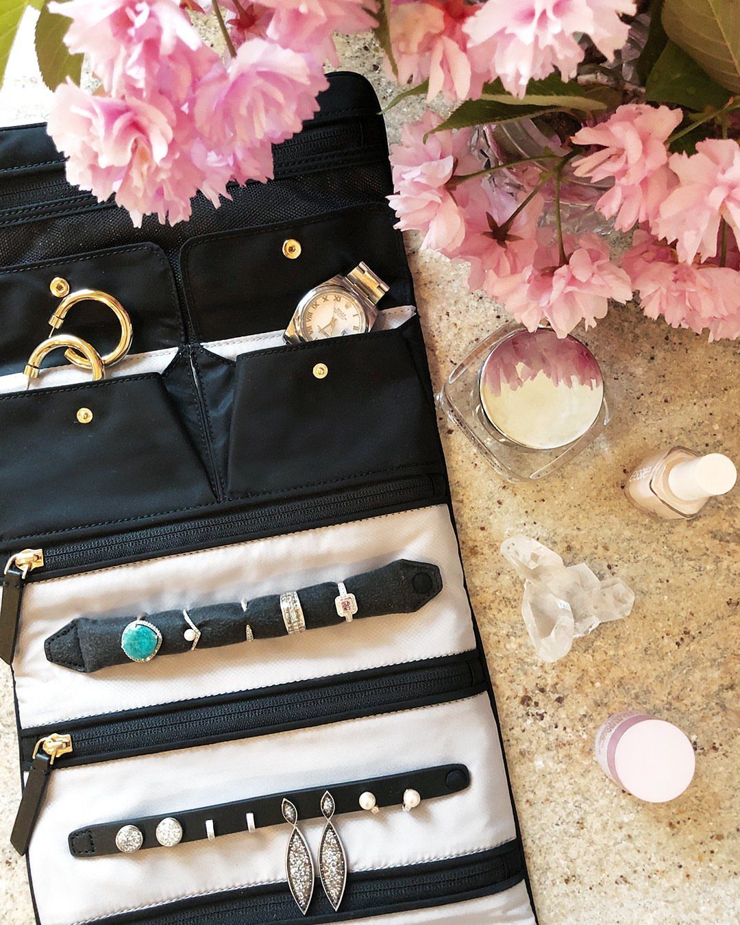 Open black and white travel jewelry roll filled with rings, earrings, and a watch.