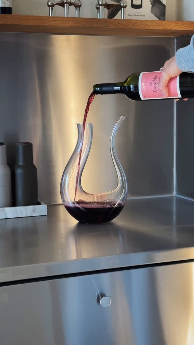 Red wine being poured from a bottle into a curved glass decanter.