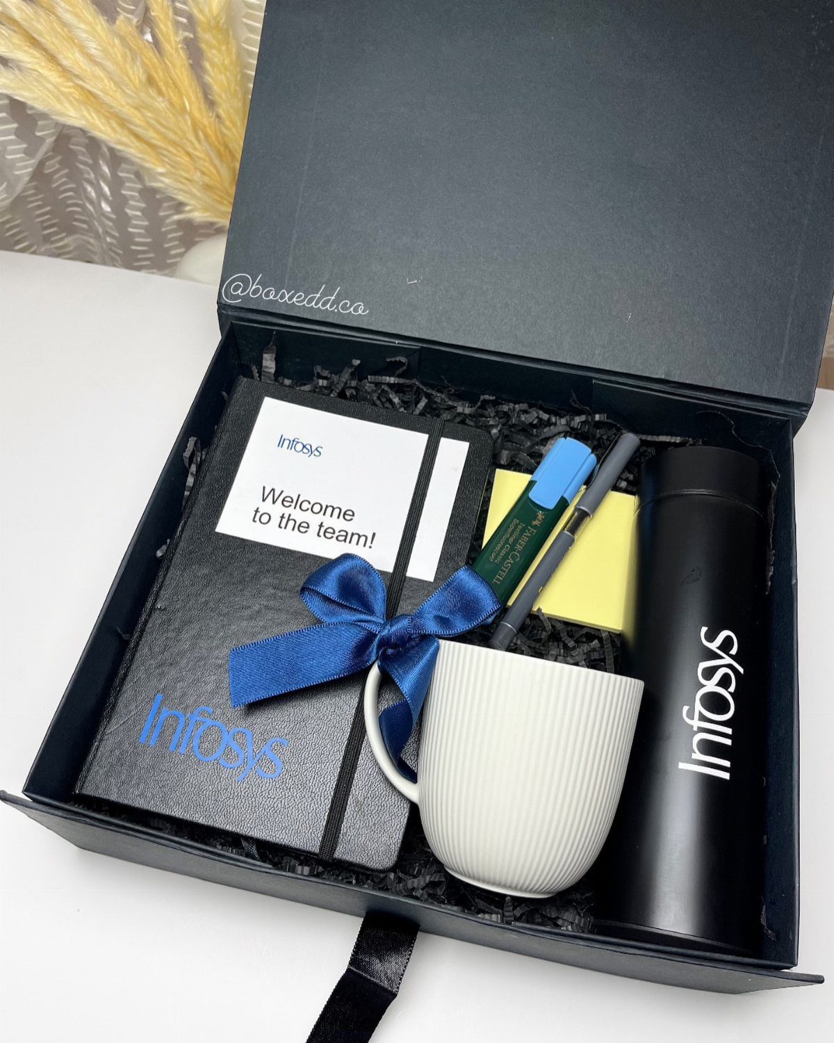 Black gift box with corporate branded notebook, mug, thermos, and welcome card.