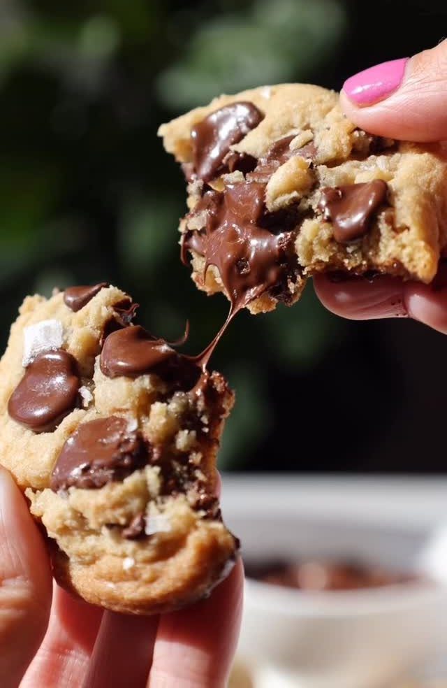 Chocolate chip cookie being pulled apart with melted chocolate stretching between pieces