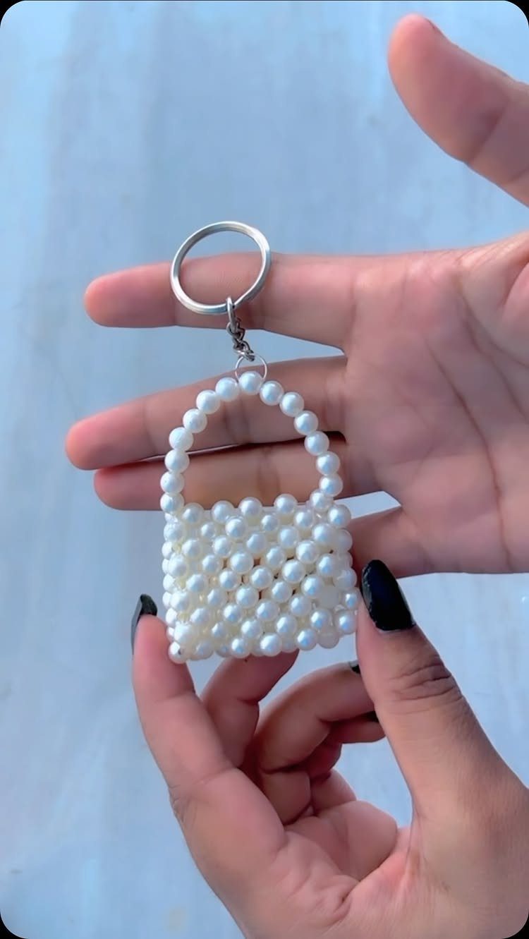 Miniature white pearl handbag keychain held by hands against a light blue background.