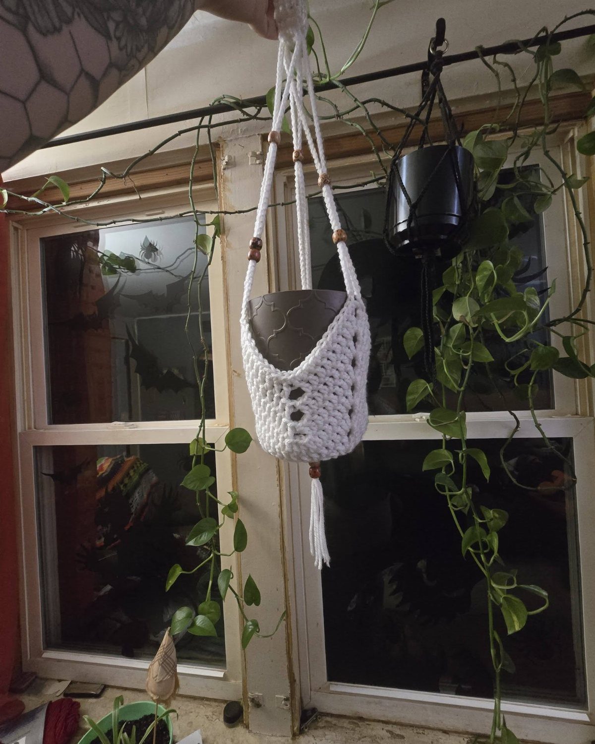 White macrame plant hanger holding a grey pot in front of a window