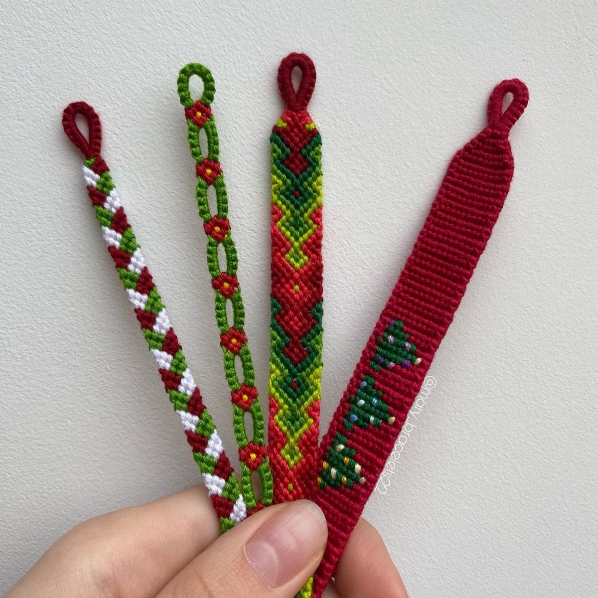 Four woven friendship bracelets in red, green, and white held by a hand.