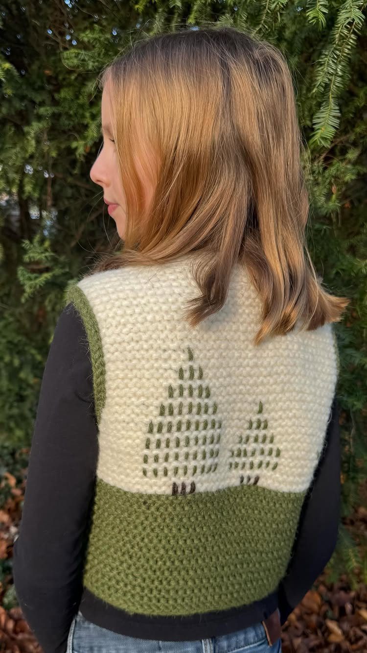 Person wearing a handmade knitted cream and olive green vest with tree patterns.
