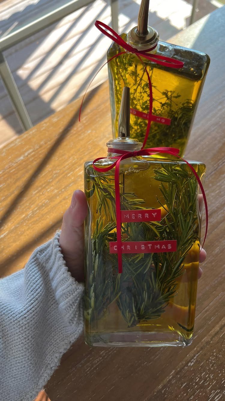 Two glass bottles of rosemary infused oil with red ribbons and Christmas labels.