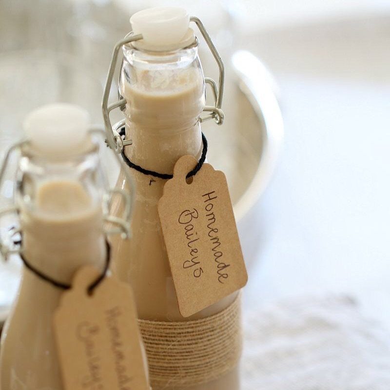 Two glass bottles of homemade Baileys liqueur with kraft paper tags and twine.