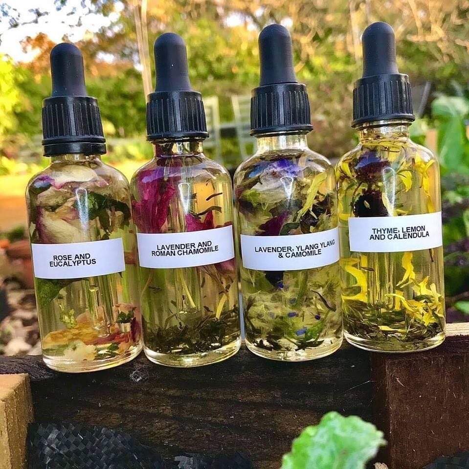 Four glass dropper bottles containing infused oils with dried botanical petals and herbs.