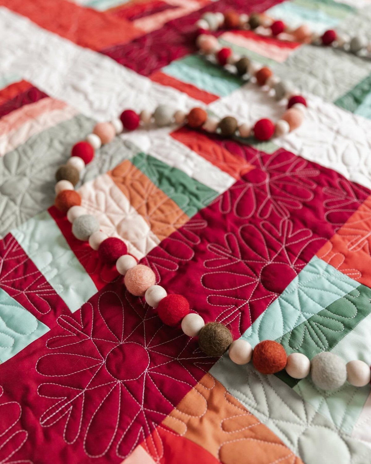 Colorful felted wool ball garland resting on a red and green quilted blanket.